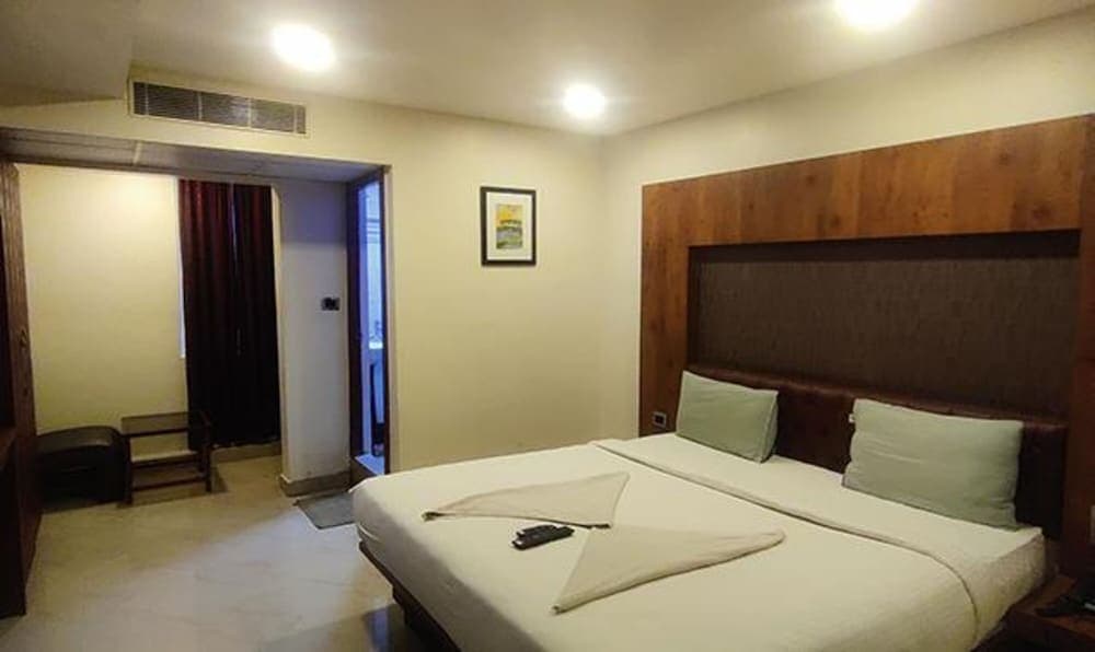 A cozy hotel room features a neatly made bed with green pillows, wooden accents, and a small seating area, ideal for travelers seeking comfort and relaxation.