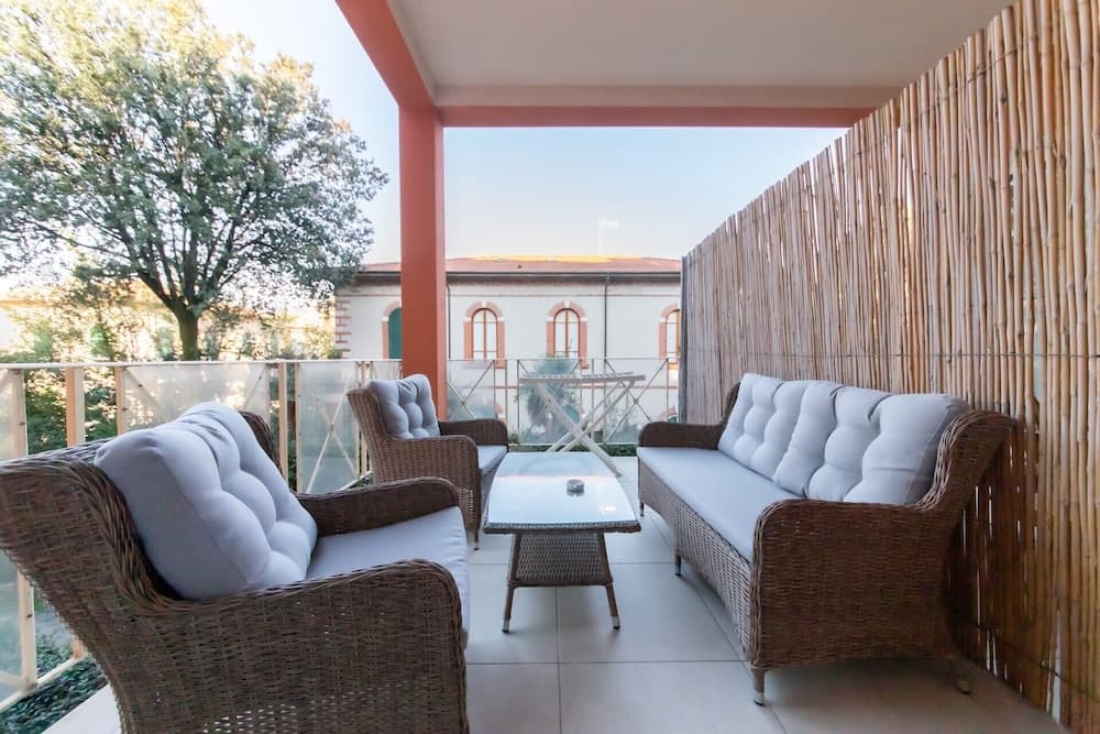A cozy balcony with wicker furniture and plush cushions offers a serene retreat, perfect for travelers seeking relaxation amidst greenery and classic architecture.