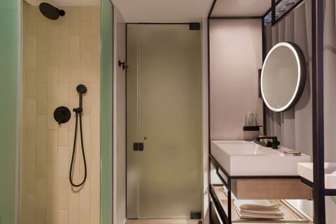 A modern bathroom in the Renaissance New York Flushing Hotel features sleek fixtures, a glass-enclosed shower, and a well-lit vanity area, ideal for travelers seeking comfort and style during their stay.