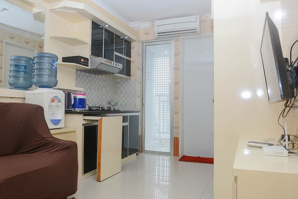 A cozy apartment kitchenette with modern appliances, water dispensers, and a mounted TV creates a welcoming atmosphere ideal for short-term travelers seeking comfort and convenience.