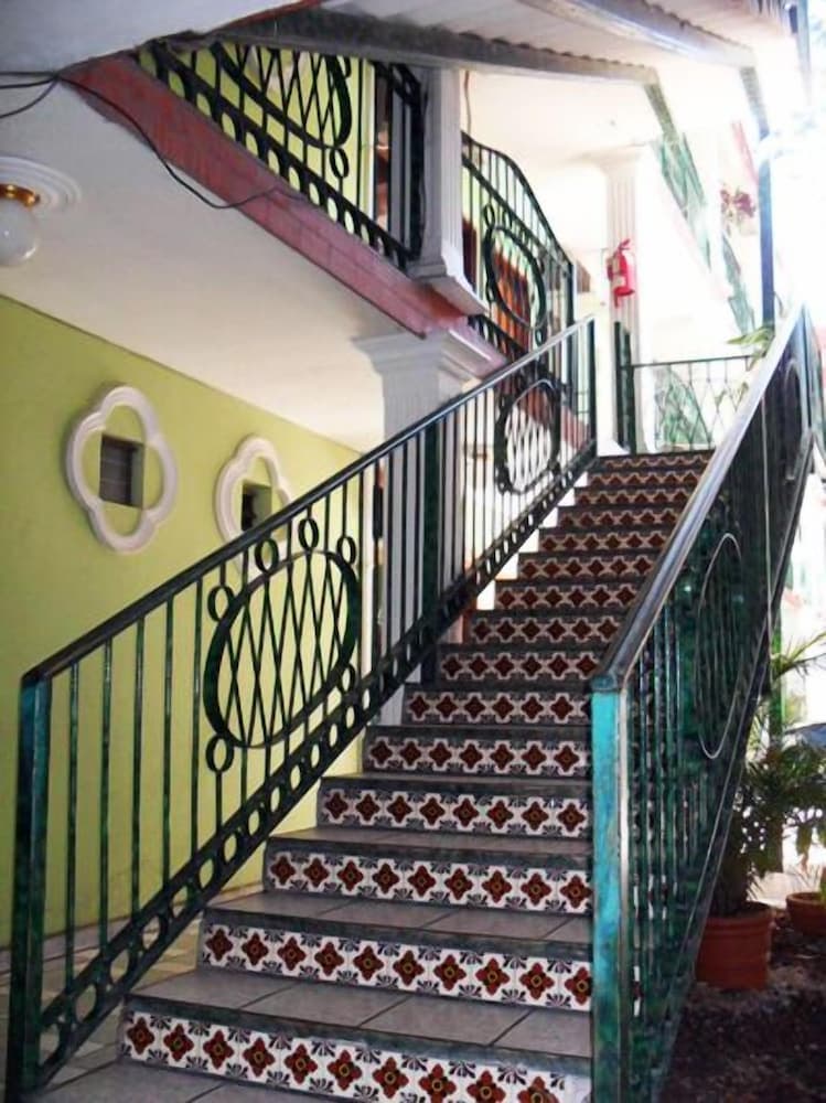 A vibrant staircase adorned with patterned tiles and ornate green railings ascends through a cozy indoor space, ideal for travelers seeking charming accommodations with a touch of local artistry.