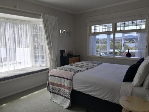 A cozy bedroom with a neatly made bed, soft natural light filtering through sheer curtains, and a scenic view of water and distant hills, ideal for travelers seeking relaxation in a serene lakeside retreat.
