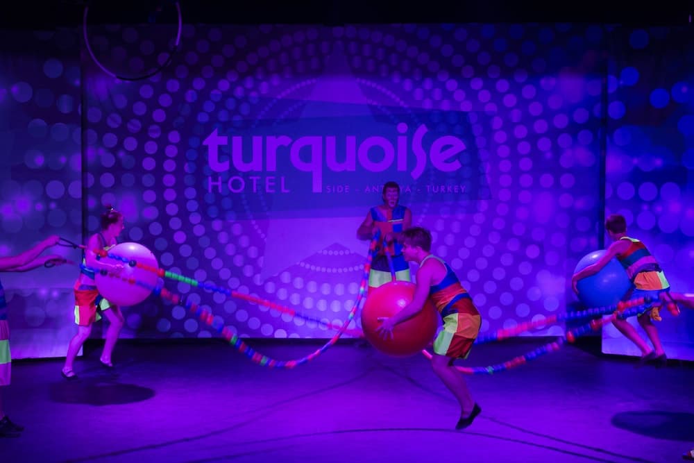 A vibrant stage performance at the Turquoise Hotel in Side, Antalya, Turkey, features colorful costumes, giant balls, and dynamic ropes, creating an energetic and playful atmosphere ideal for family entertainment.