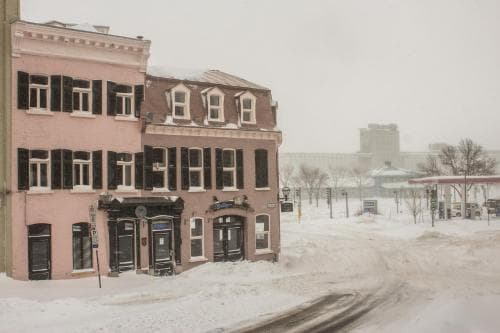 A serene winter scene captures a quaint pink building with black shutters along a snow-covered street, ideal for travelers seeking cozy urban retreats in chilly destinations.