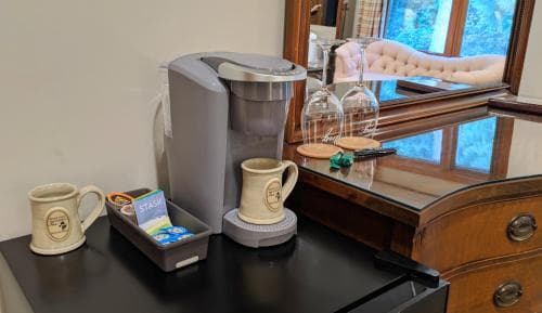 A cozy hotel room corner features a sleek coffee maker setup with mugs and tea packets on a polished black table, reflecting a warm and inviting atmosphere ideal for travelers seeking comfort and convenience.