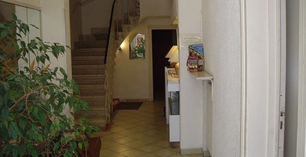 A cozy hotel lobby with tiled floors, a staircase, indoor plants, and a reception desk creates a welcoming atmosphere ideal for travelers seeking comfort and convenience.