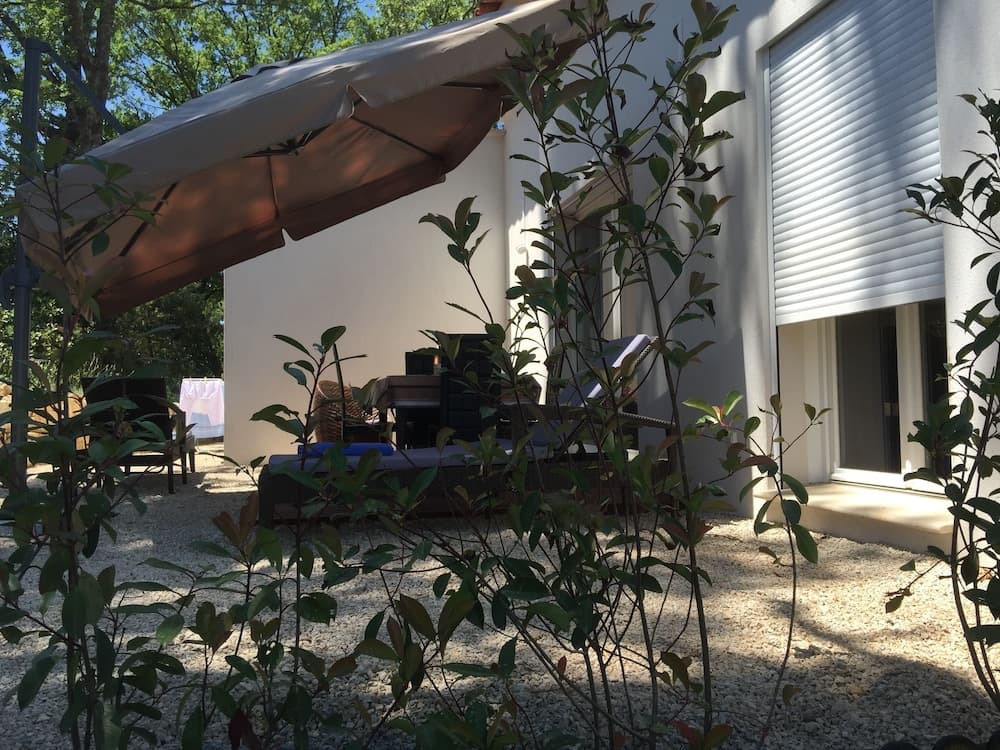 A serene outdoor patio shaded by a beige awning features comfortable lounge chairs amidst lush greenery, ideal for relaxing retreats in a tranquil residential setting.