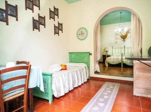 A cozy Mediterranean-style bedroom with terracotta flooring, pastel green furniture, and an arched doorway leading to another room, ideal for travelers seeking a charming and relaxing retreat.