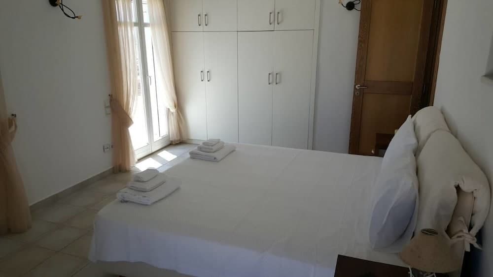 A serene hotel bedroom features a neatly made bed with white linens, a large wardrobe, soft curtains framing a bright window, and a cozy ambiance ideal for travelers seeking relaxation.