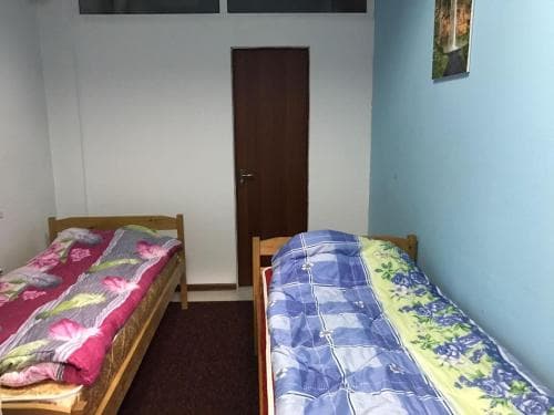 A cozy budget-friendly hostel room features two single beds with colorful quilts against light blue walls, ideal for solo travelers seeking simple accommodations.