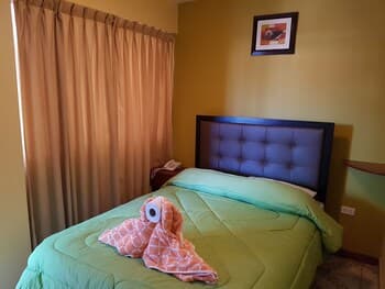 A cozy bedroom with a neatly made bed adorned with a playful plush octopus, warm curtains, and soft lighting creates an inviting atmosphere ideal for travelers seeking comfort and relaxation.