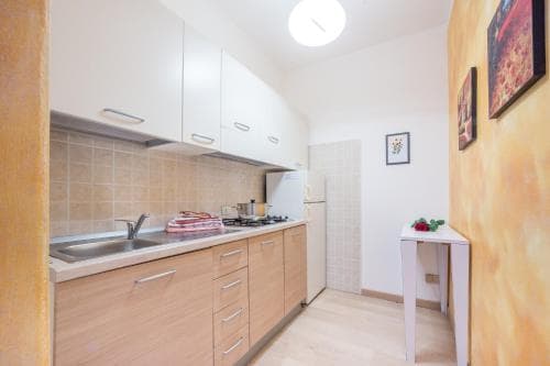 A cozy apartment kitchen with wooden cabinets, white countertops, and warm yellow walls creates an inviting atmosphere, perfect for travelers seeking a homey cooking space during their stay.