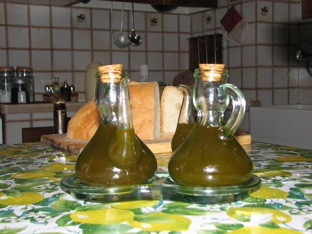 A cozy kitchen scene features two glass bottles of olive oil on a vibrant lemon-patterned tablecloth, alongside fresh bread, evoking a rustic culinary atmosphere ideal for travelers seeking authentic local dining experiences.
