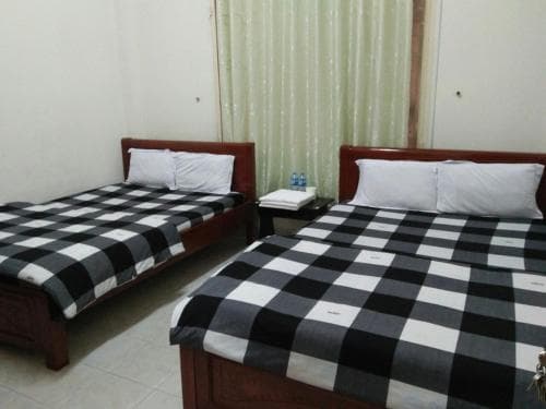 A cozy budget hotel room features two wooden beds with striking black-and-white checkered bedding, set against a backdrop of soft curtains, ideal for travelers seeking simple accommodations.