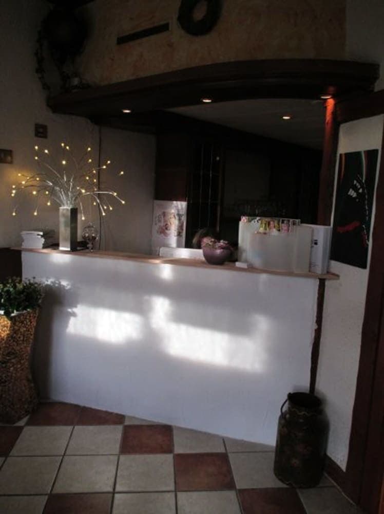 A cozy hotel reception area features a white counter adorned with decorative lights and plants, set against warm-toned walls and checkered flooring, ideal for travelers seeking a welcoming and intimate check-in experience.