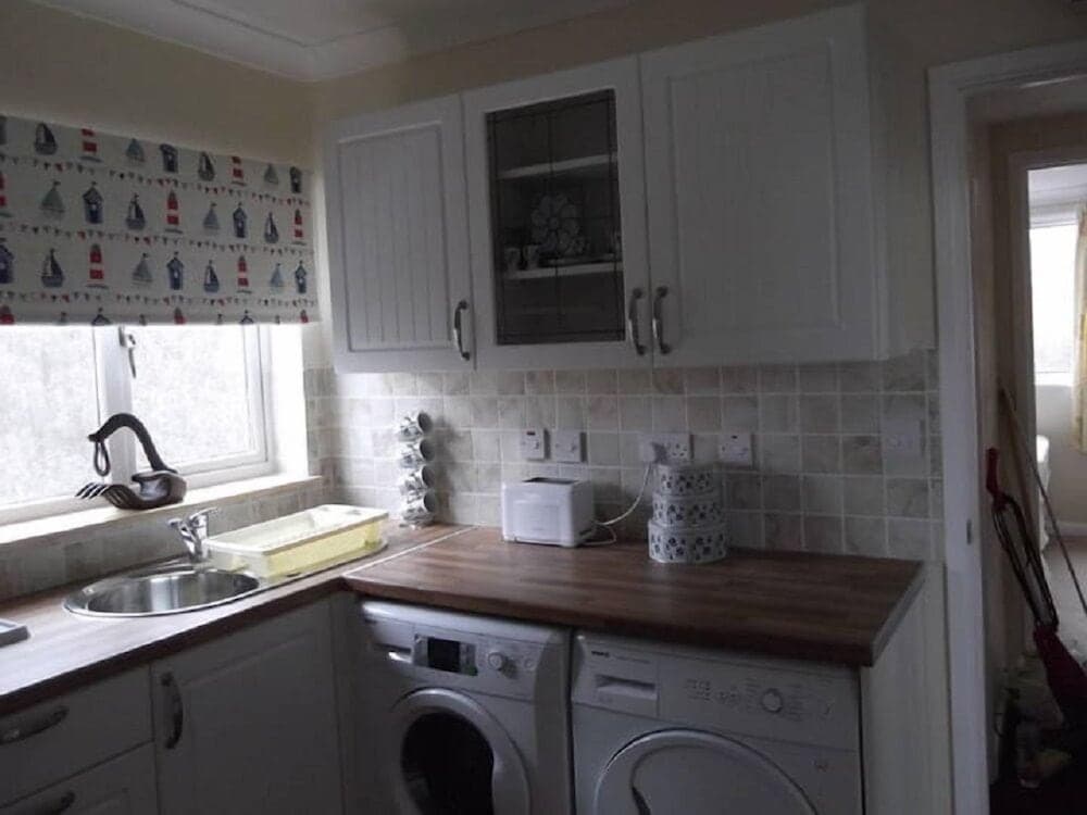 A cozy kitchen with white cabinetry, wooden countertops, and a lighthouse-themed curtain exudes a homely vibe, perfect for travelers seeking a self-catering accommodation experience.