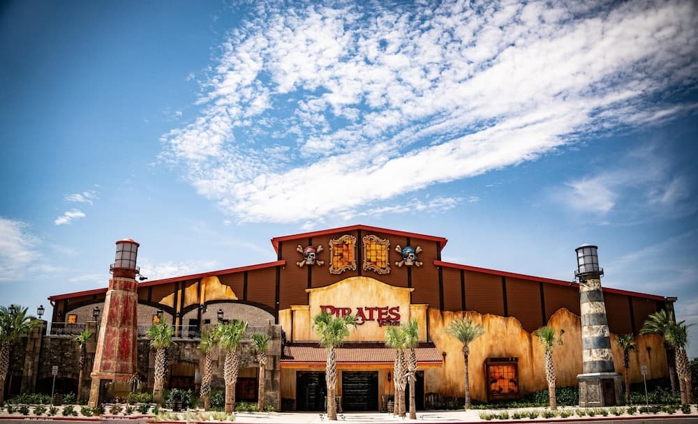 A vibrant pirate-themed amusement park entrance under a bright blue sky features skull decorations, palm trees, and lighthouse towers, ideal for family vacation planning.