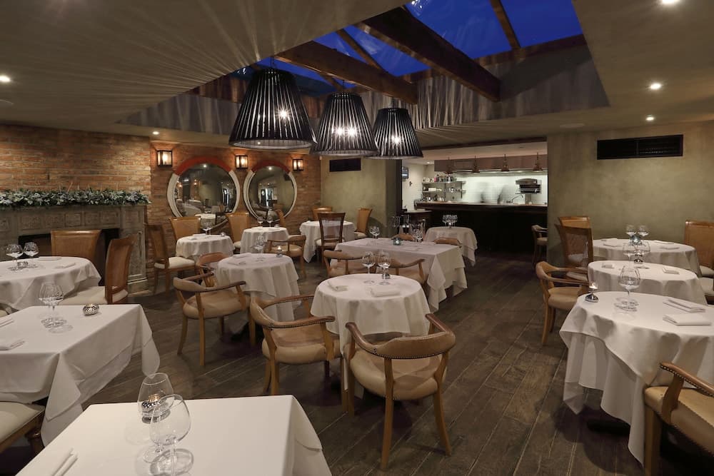 An elegant indoor dining area with cozy wooden floors, white tablecloths, warm lighting from black pendant lamps, and a brick wall adorned with mirrors, perfect for a romantic evening or special occasion.