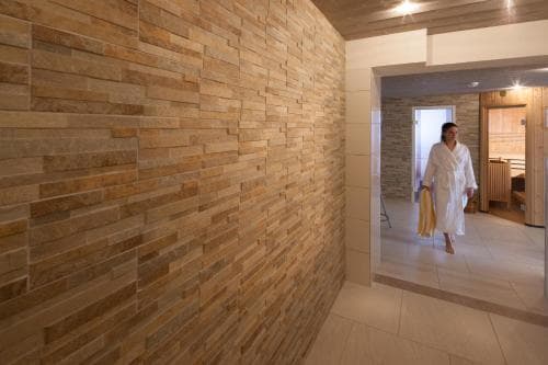A serene spa hallway with warm stone walls and soft lighting sets a tranquil mood as a woman in a white robe carries yellow towels, ideal for relaxation and wellness retreats.