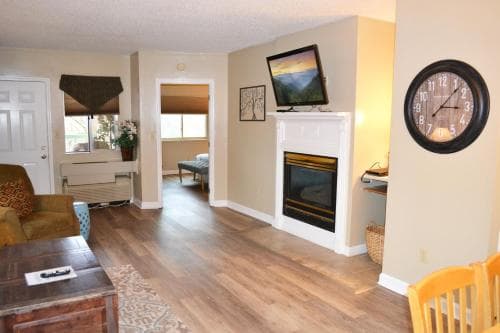 A cozy living room with warm wooden floors, a fireplace adorned with artwork, and inviting furniture creates a welcoming atmosphere ideal for a relaxing vacation rental stay.