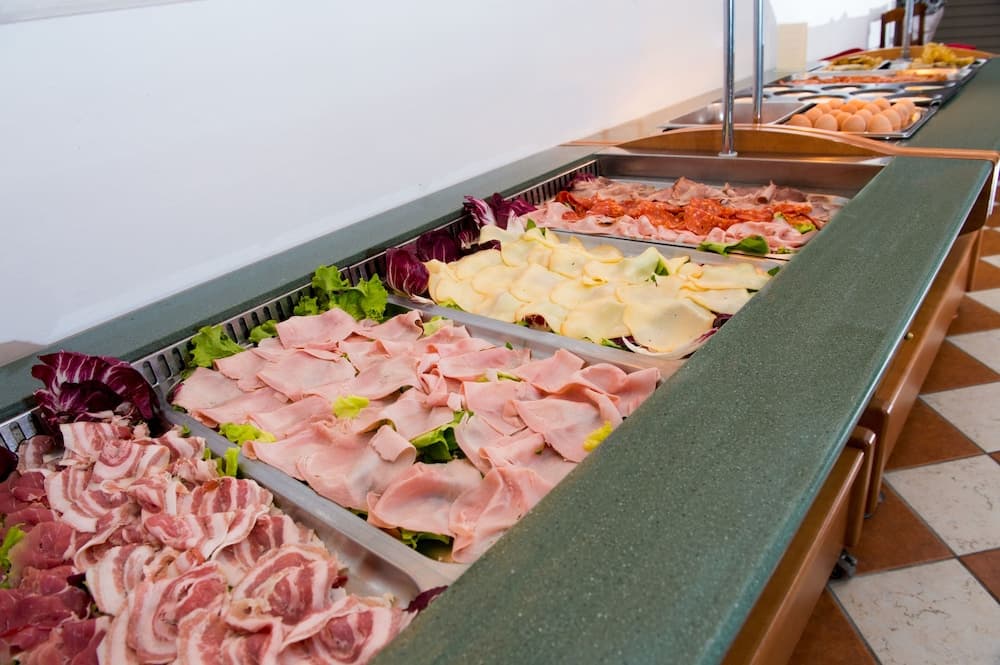 A vibrant buffet spread featuring neatly arranged cured meats, cheeses, and fresh greens invites travelers to indulge in a hearty meal at a cozy dining area.