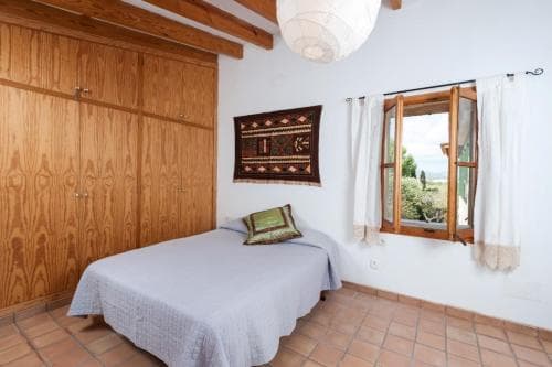 A cozy bedroom with terracotta tiled floors, wooden furnishings, and a window offering a serene view of greenery, ideal for travelers seeking a tranquil retreat in a rustic villa.