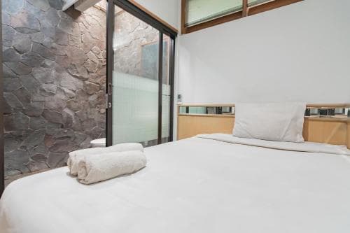 A cozy bedroom with a neatly made bed, stone accent wall, and modern glass sliding door exudes a serene atmosphere, ideal for travelers seeking a tranquil retreat in a boutique hotel setting.