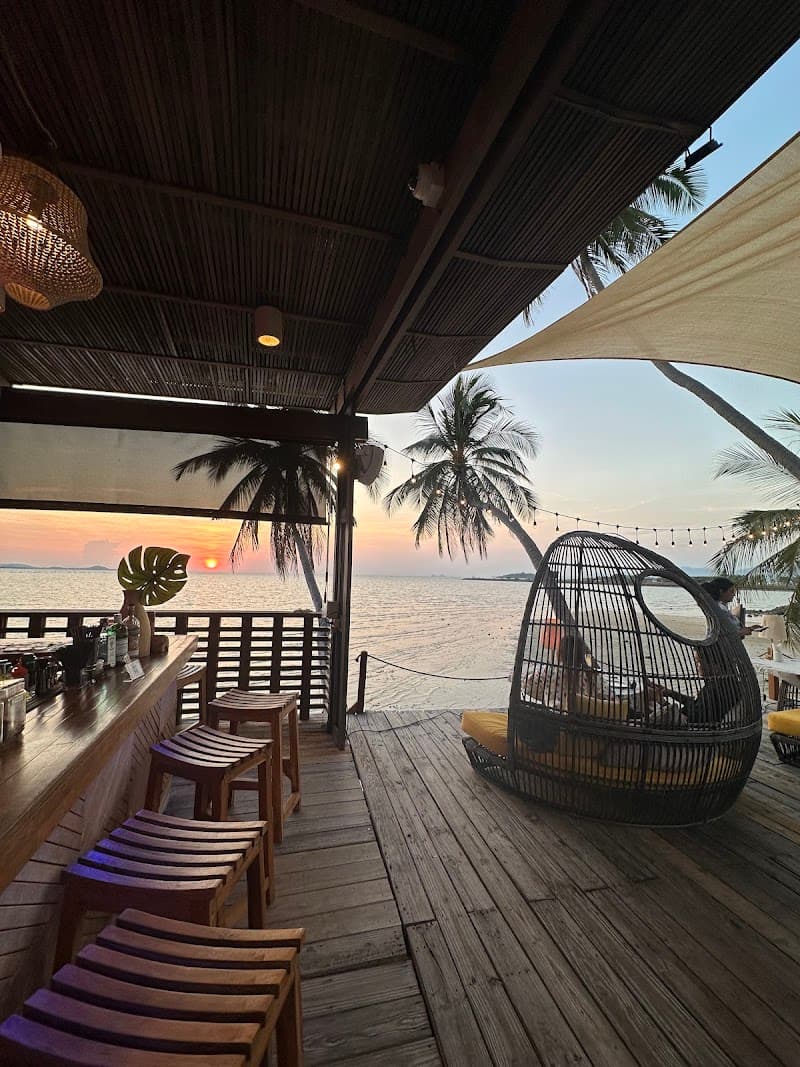A serene beachside bar at sunset offers cozy seating and stunning ocean views, perfect for travelers seeking relaxation on Ko Samui, Thailand.