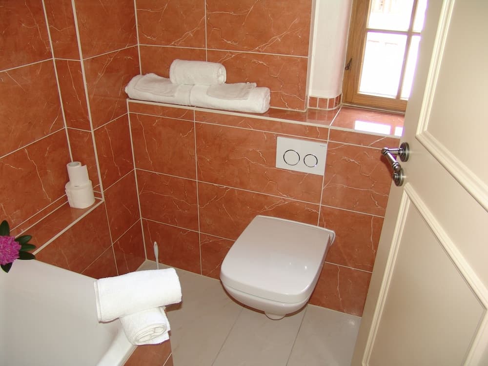 A cozy bathroom with warm terracotta tiles, neatly folded white towels, and a small window, ideal for travelers seeking comfort and cleanliness in their accommodations.