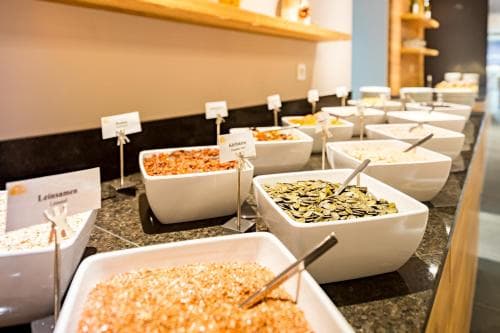 A cozy hotel breakfast buffet displays an array of cereals and seeds in neatly arranged white bowls, inviting travelers to start their day with a nutritious meal.