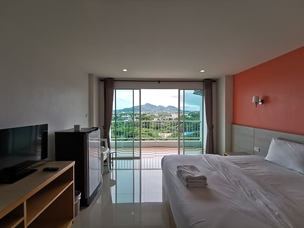 A cozy hotel room with a vibrant orange accent wall, modern furnishings, and a serene balcony view of lush greenery and distant mountains, ideal for travelers seeking relaxation and scenic vistas.