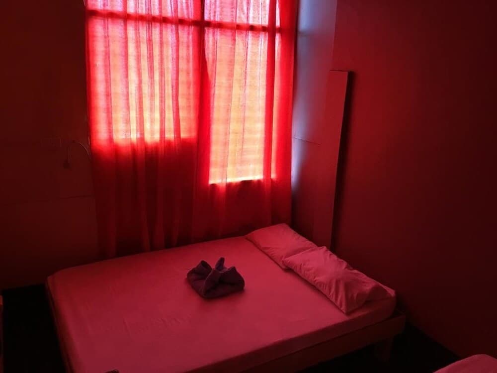 A cozy bedroom with vibrant red walls and curtains bathes in warm sunlight, featuring a neatly made bed with folded towels, ideal for travelers seeking a serene and intimate retreat.