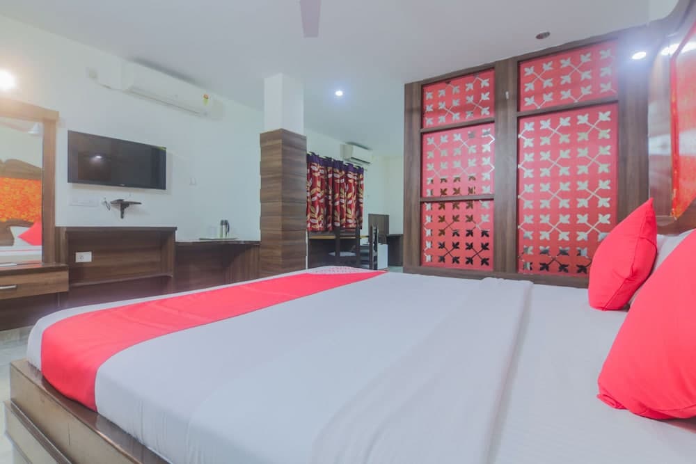 A cozy hotel room features a neatly made bed with red accents, wooden furnishings, a flat-screen TV, and vibrant red patterned sliding doors, ideal for travelers seeking comfort and style.