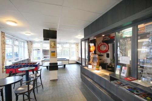 A cozy indoor café with bright windows, pool tables, and a counter displaying brochures invites travelers seeking relaxation and entertainment in a casual setting.