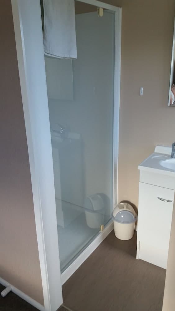 A cozy hotel bathroom features a glass-enclosed shower, white vanity sink, and beige walls, creating a clean and functional space ideal for travelers seeking comfort and convenience.