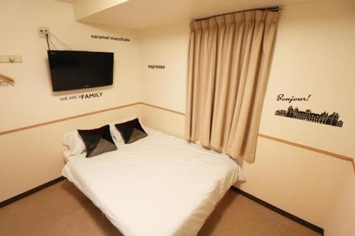 A cozy hotel room features a neatly made bed, a wall-mounted TV, and decorative coffee-themed decals, creating a welcoming atmosphere ideal for travelers seeking comfort and relaxation.