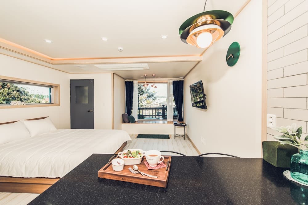 A cozy modern bedroom with a neatly made bed, a dining area featuring a tray of food, and a balcony view through large windows, ideal for travelers seeking comfort and relaxation in a stylish retreat.