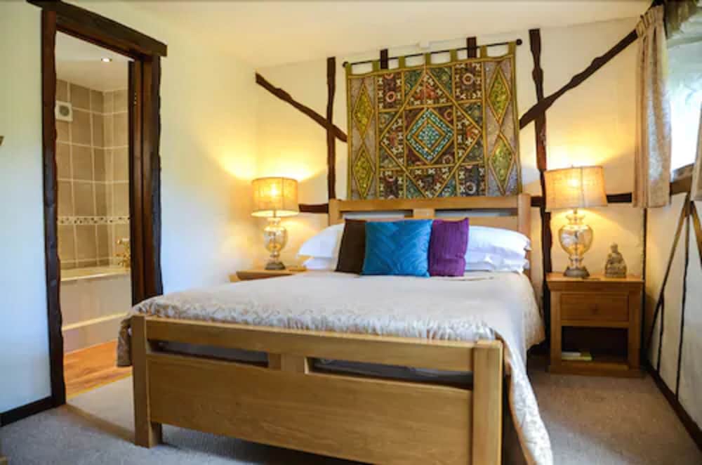 A cozy bedroom with rustic wooden beams, a vibrant tapestry above the bed, and warm lighting creates an inviting atmosphere, perfect for travelers seeking a charming and comfortable retreat.