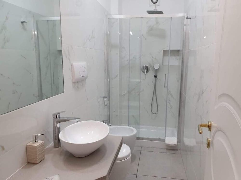 A modern, clean bathroom with marble tiles, a glass-enclosed shower, a sleek sink, and a large mirror creates a serene atmosphere ideal for travelers seeking comfort and style in their accommodations.