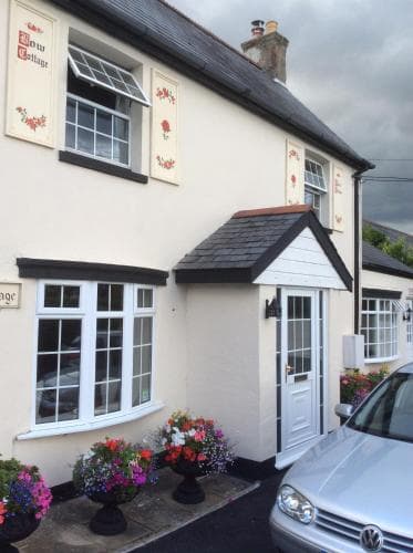 A charming, cozy cottage with vibrant flower pots and quaint decor invites travelers to explore its serene village setting, perfect for a relaxing getaway.