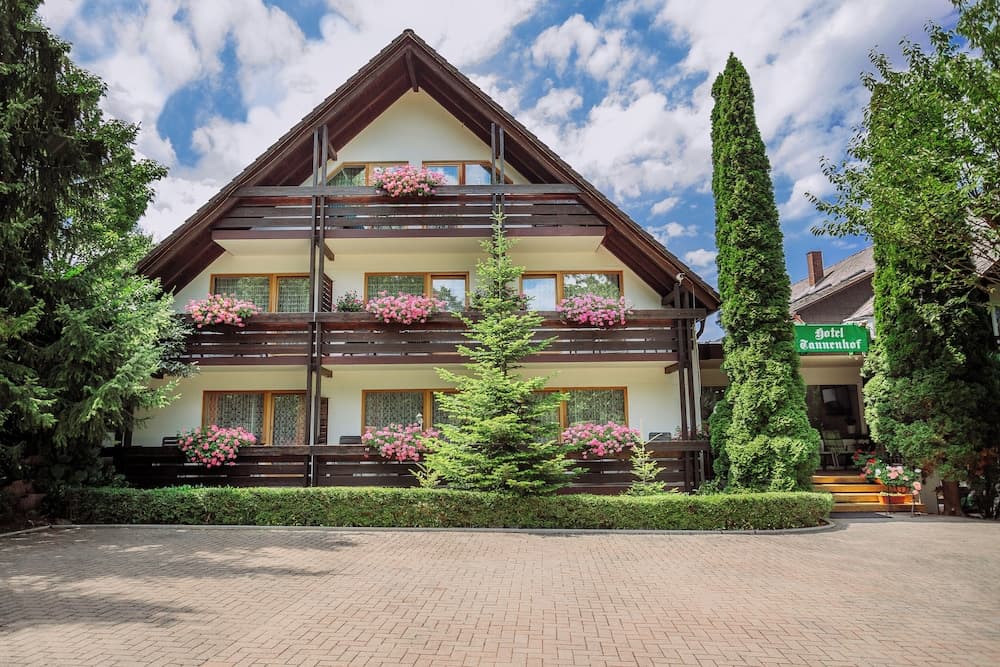A charming two-story hotel adorned with vibrant pink flowers and lush greenery under a bright blue sky, ideal for travelers seeking a serene and picturesque accommodation experience.