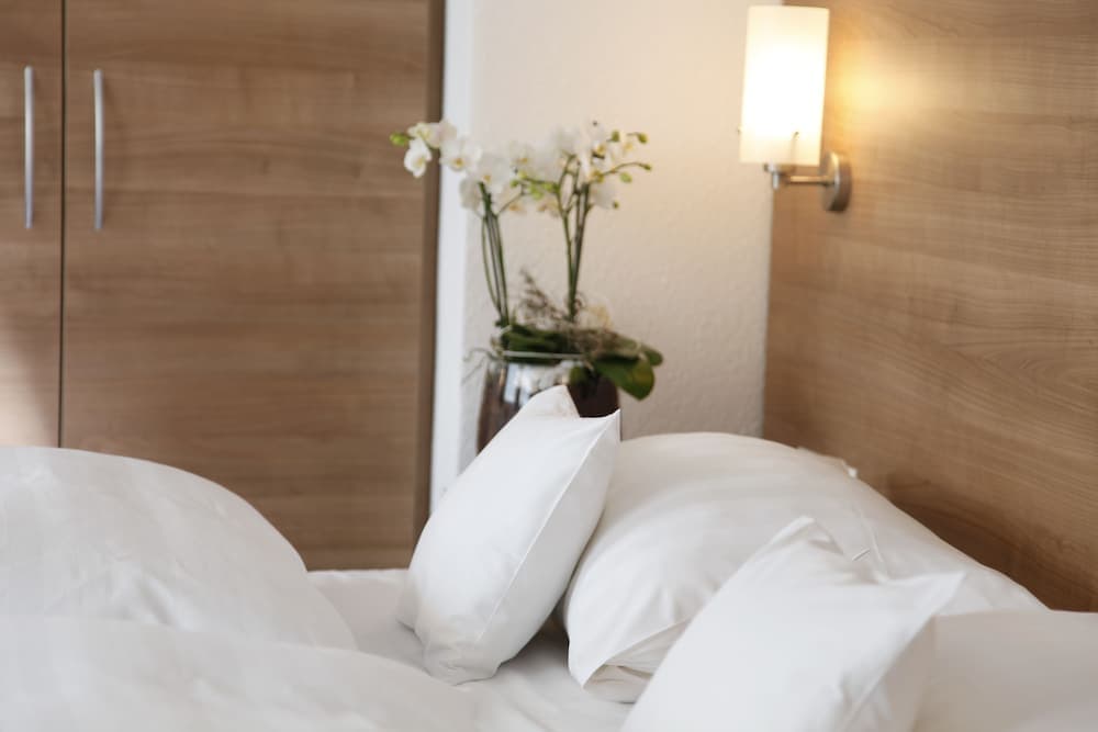 A cozy hotel bedroom features a neatly made bed with white linens, a soft-lit wall sconce, and a vase of fresh orchids, ideal for travelers seeking comfort and relaxation.