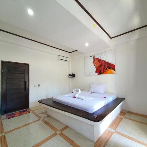 A serene hotel room features a raised bed adorned with swan towels and rose petals, set against tiled floors and a vibrant wall art piece, ideal for travelers seeking a cozy and artistic retreat.