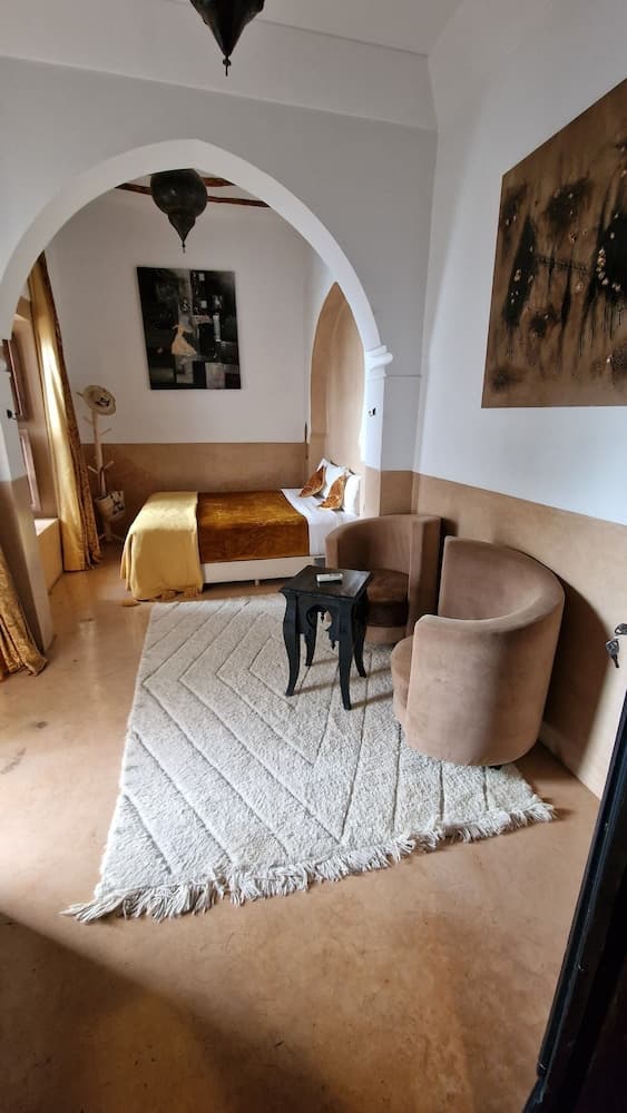 A cozy, warmly lit boutique hotel room features an inviting bed draped in golden linens, plush armchairs on a textured rug, and artistic wall decor, perfect for travelers seeking a serene and stylish retreat.