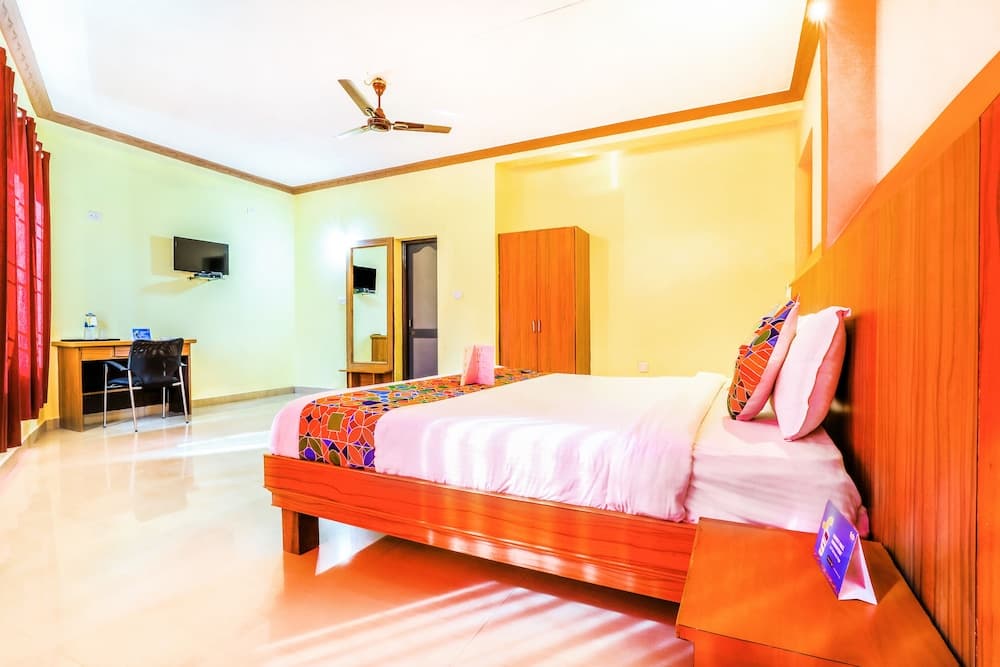 A cozy hotel room features a neatly made bed with colorful pillows, wooden furniture, a flat-screen TV, and vibrant red accents, ideal for travelers seeking comfort and convenience.