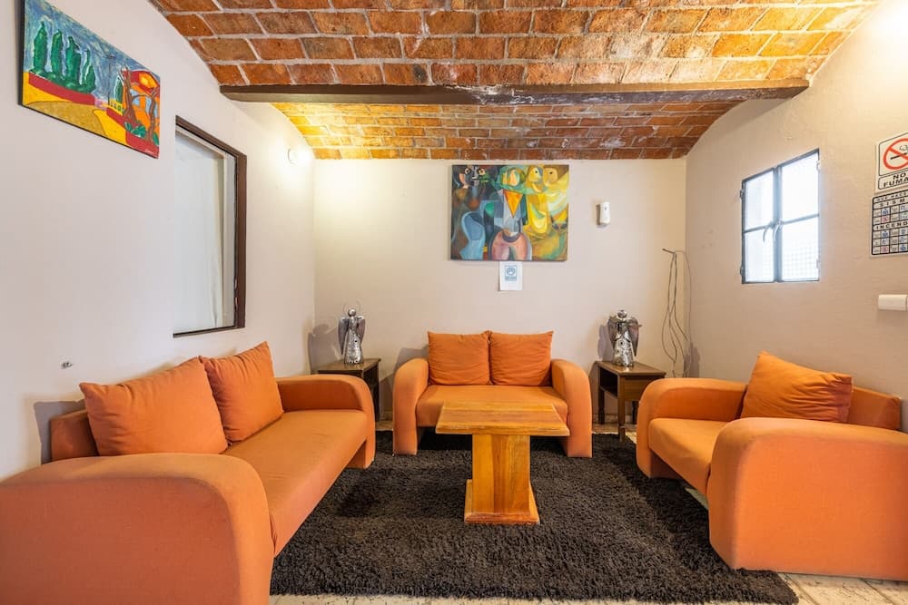 A cozy lounge area with vibrant orange seating, exposed brick arches, and colorful artwork creates an inviting atmosphere ideal for travelers seeking a relaxing retreat.