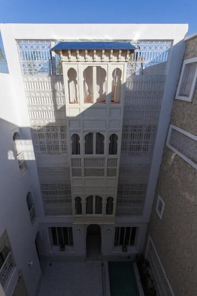 A serene courtyard with traditional Islamic architecture featuring arched windows, intricate latticework, and a small pool, ideal for cultural heritage tourism and photography.