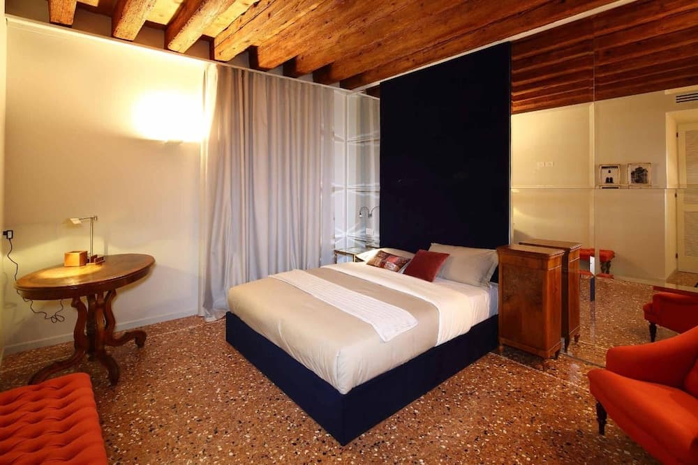 A cozy hotel room with rustic wooden beams, terrazzo flooring, and vibrant red accents offers a warm and inviting atmosphere ideal for travelers seeking comfort and charm.