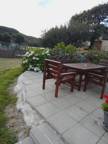 A serene outdoor patio features wooden furniture surrounded by vibrant flowers and lush greenery, ideal for a relaxing getaway in a tranquil garden setting.