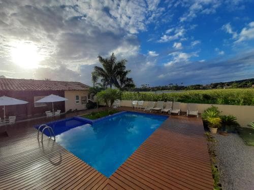 A serene villa with a sparkling pool, wooden deck, lounge chairs, and tropical plants under a vibrant sky, ideal for a relaxing vacation retreat.